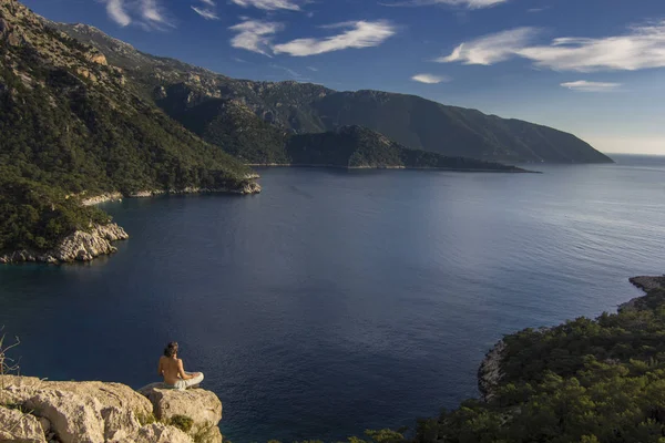 Hombre sentado en un acantilado en las montañas cerca del mar mediterráneo —  Fotos de Stock