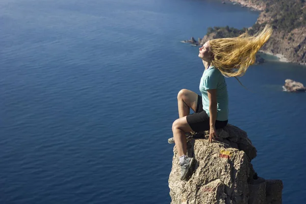 Flicka sitter på en klippa i bergen nära Medelhavet med fladdrande hår — Stockfoto