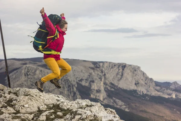 Mädchen mit Rucksack springt auf Klippe in den Bergen — Stockfoto