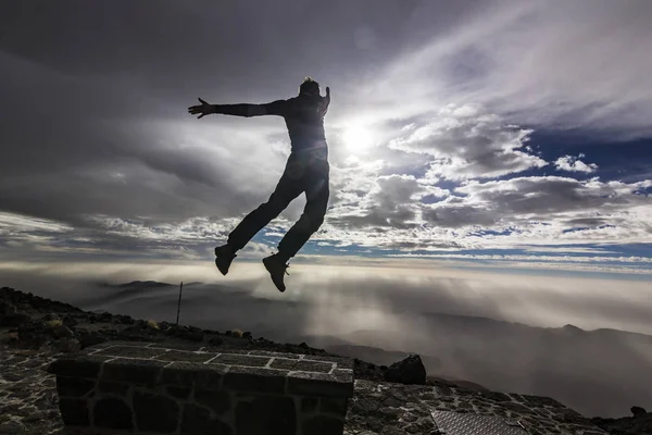 Homem pulando com as mãos para cima sol oposto com nuvens no céu — Fotografia de Stock