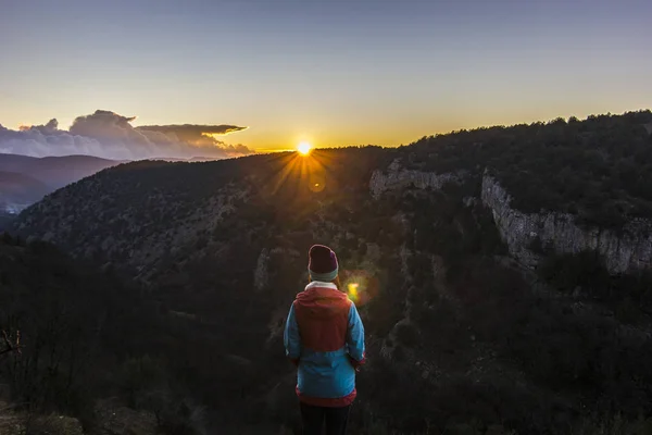 Mädchen steht bei Sonnenuntergang auf einer Klippe in den Bergen — Stockfoto