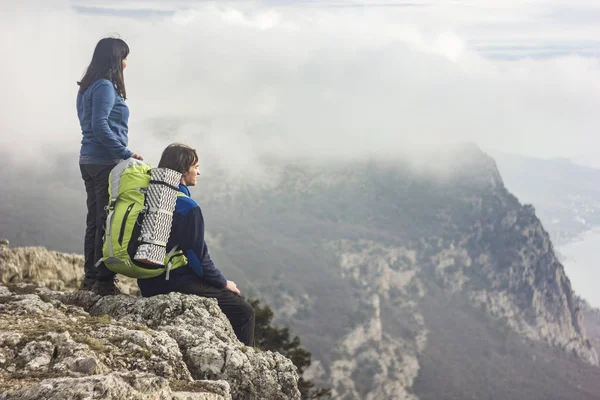 Casal sentado em um penhasco em montanhas olhando para a frente — Fotografia de Stock