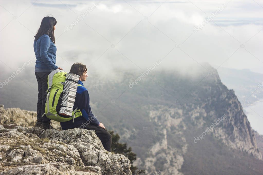 couple sitting on a cliff in mountains looking forward