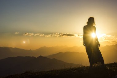 Silhouete bir kız elbise ayakta günbatımı dağlarda çimenlerin üzerinde