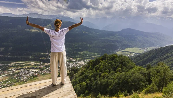 Meisje in witte t-short met handen omhoog staande op gras in zonsondergang bergen — Stockfoto