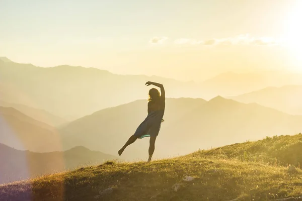 Mädchen in Kleid mit Händen nach oben tanzen auf Gras in den Bergen des Sonnenuntergangs — Stockfoto