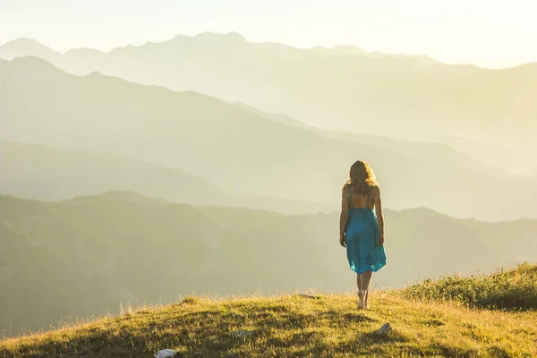 Menina de vestido em pé na grama em montanhas pôr do sol — Fotografia de Stock