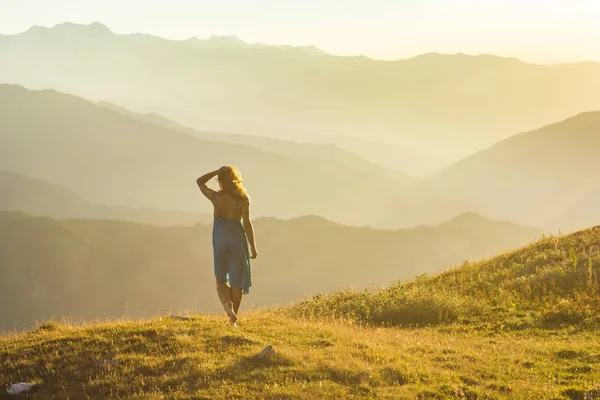 Meisje met jurk tegoed op gras in zonsondergang bergen — Stockfoto