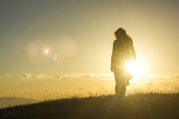 Silhouete flicka i klänning står på gräset i solnedgången berg — Stockfoto