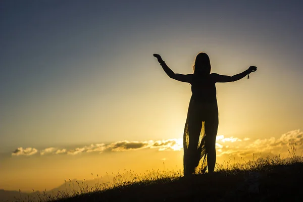 Silhueta de menina de vestido em pé na grama em montanhas pôr do sol — Fotografia de Stock