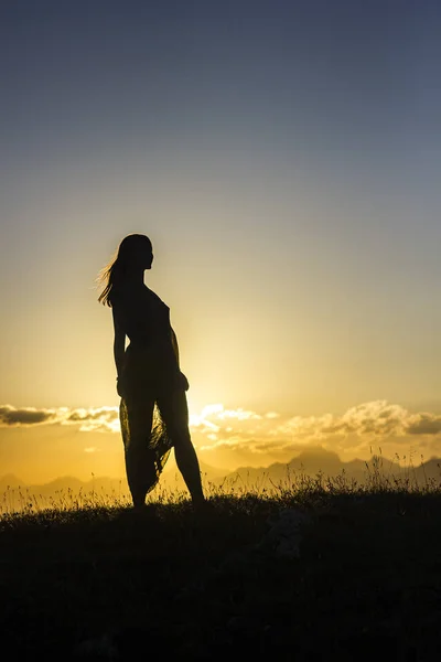 Silhouete flicka i klänning står på gräset i solnedgången berg — Stockfoto