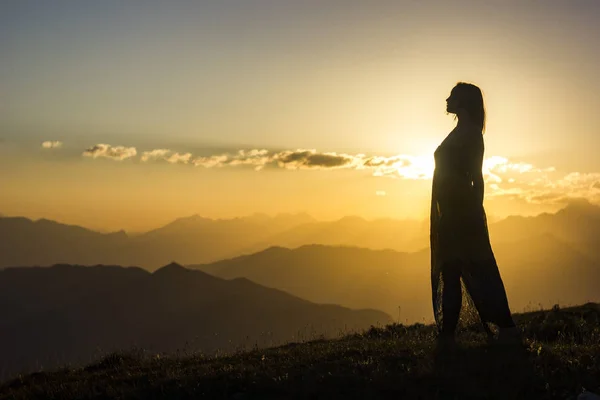 Silhouete flicka i klänning står på gräset i solnedgången berg — Stockfoto