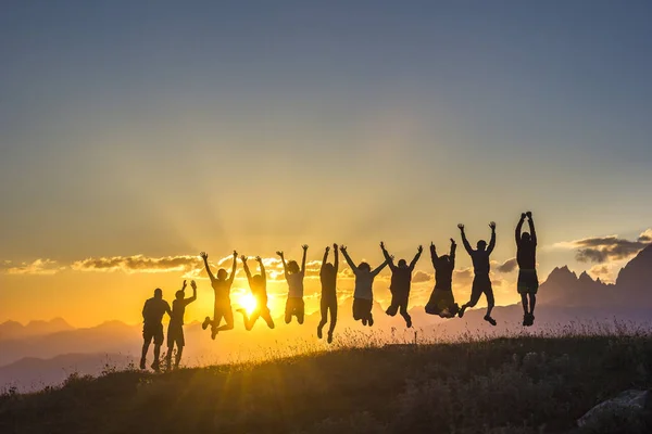 Grupo de personas con las manos arriba saltando sobre la hierba en las montañas del atardecer Fotos de stock libres de derechos