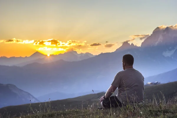Mann sitzt auf Gras bei Sonnenuntergang in den Bergen Stockfoto