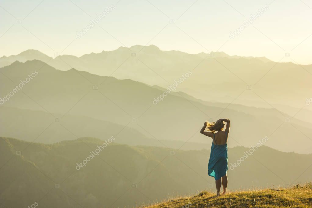 girl in dress standing on grass in sunset mountains