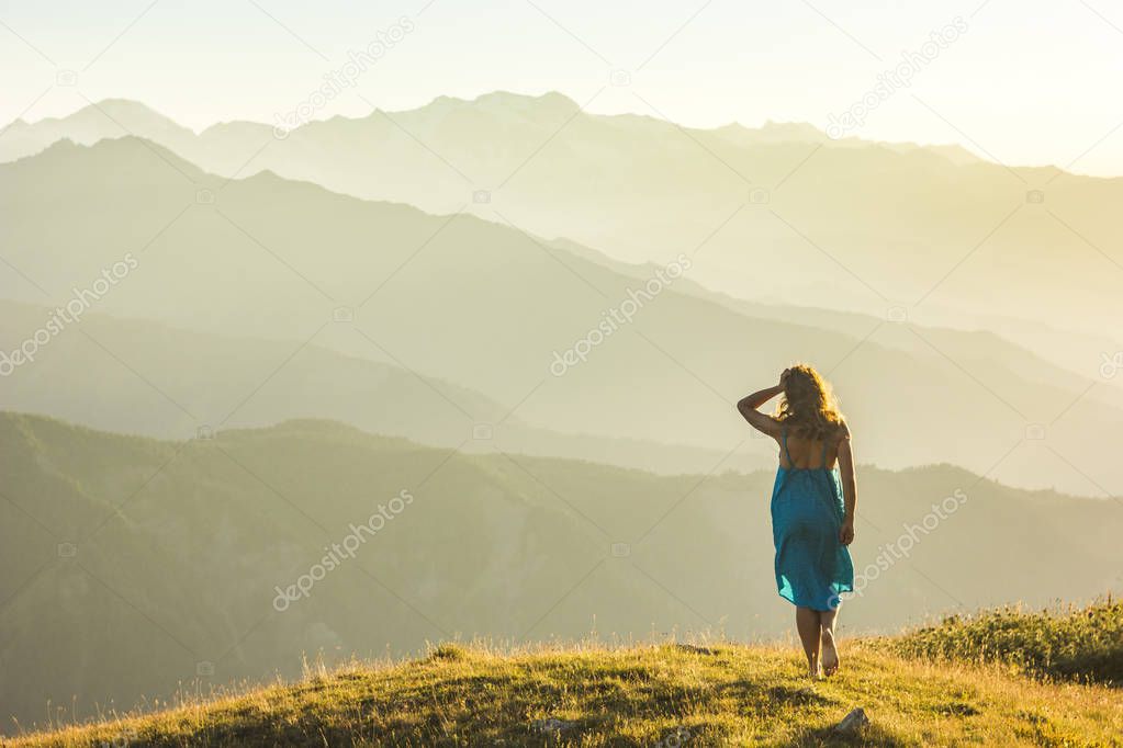 girl in dress standing on grass in sunset mountains