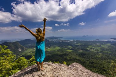 Eller yukarı dağlar aşağıdaki gün batımında kaya üzerinde duran kızla