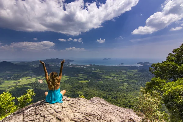 Meisje met handen omhoog zittend op de rots bij daglicht met bergen hieronder — Stockfoto
