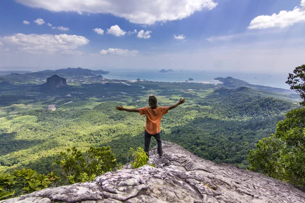 Man with hands up standing on rock at sunset with mountains below — Stock Photo, Image