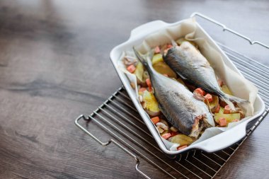 İki lezzetli ve iştah açıcı deniz balığı, ahşap bir masada patates, havuç, soğan ve sarımsak ile pişirilmiş. Ev yapımı lezzetli ve basit yiyecekler. Fırında balık pişiyor. Üst görünüm 