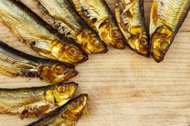 Tahta kesme tahtasına yerleştirilmiş altın sarısı tütsülenmiş balıklar.