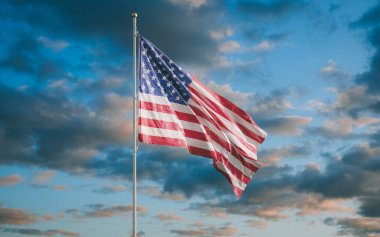 Rüzgarda dalgalanan güzel bir Amerikan bayrağı günbatımı gökyüzünün arka planında. Eski Zafer, Yıldızlar ve Çizgiler olarak bilinen Amerikan gururunun sembolü.