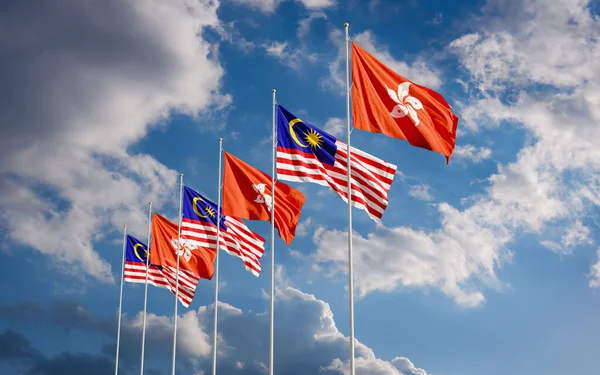 The Malaysian and Hong Kong flags fly together in the wind against the blue sky. The concept of cooperation and competition in economics and politics. Flag of the Malaysia to the left of Hong Kong.
