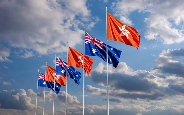 The Aussie and Hong Kong flags fly together in the wind against the cloudy blue sky background. The concept of cooperation and competition in economics and politics. Flag of the Australia to the left of Hong Kong.