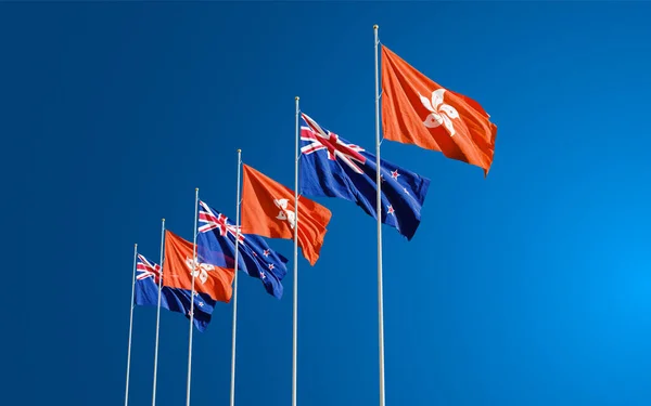 The New Zealand and Hong Kong flags fly together in the wind against the blue sky. The concept of cooperation and competition in economics and politics. Flag of the New Zealand to the left of Hong Kong.