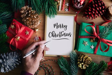 Arkaplanda hediye kutusu ve süs eşyası olan insan el yazısı kartlarının olduğu mutlu noel kavramları. Kış mevsimi aktivite fikirleri.