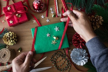 İnsan eliyle dekore edilen hediye kutusu ve ahşap masa arkasındaki süs eşyalarıyla mutlu noel kavramları. Kış mevsiminin kutlama fikirleri.