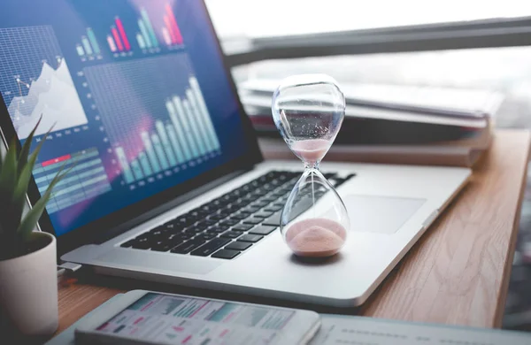 İş adamlarının bilgisayarında grafikle birlikte kum saati tuttuğu iş konseptleri. Yatırım analizi için, fikirlerin başarıya ulaşmasını bekliyor.