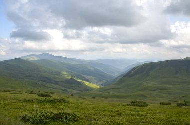 Bulutlarla dolu dramatik bir gökyüzü altında yemyeşil vadiler ve tepelerle nefes kesen dağ sırası doğayla barışçıl bir bağın altını çiziyor. Karpat Dağları, Ukrayna