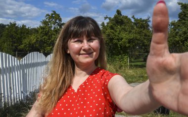 Açık havada yaşayan bir kadın, yeşil bir çitin yanında dikilip, pozitif davranışlı selfie çekiyor.