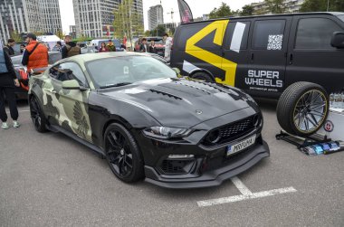 Siyah Ford Mustang Coupe, önde kamuflaj kıyafetleri var. Kaputu çoklu kepçeler, mangallar ve önden bölmeli.