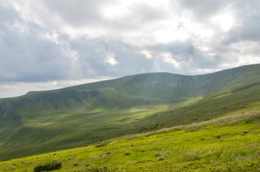 Dramatik, bulutlu gökyüzünün altındaki yemyeşil dağların güzel manzarası doğanın sükunetini ve sonsuzluğunu gösteriyor. Karpat Dağları, Ukrayna