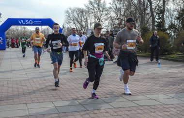 Katılımcılar, izleyiciler ve manzaralarla çevrili bir maraton etkinliği sırasında etkin bir şekilde parkta koşuyorlar.