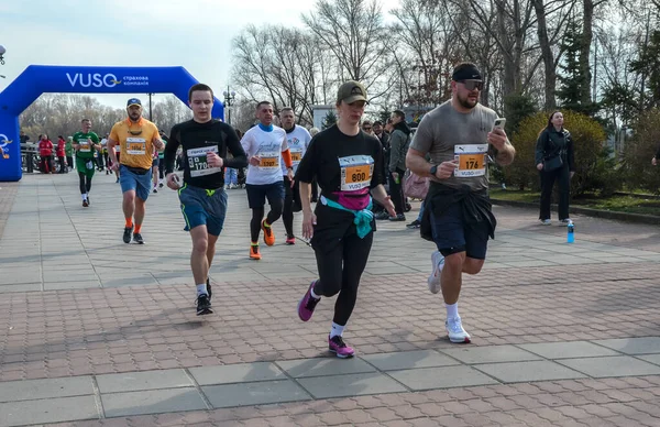 Katılımcılar, izleyiciler ve manzaralarla çevrili bir maraton etkinliği sırasında etkin bir şekilde parkta koşuyorlar.