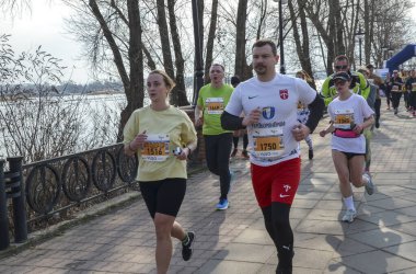 Bir maraton etkinliğinde nehir kenarında koşan bir grup sporcu, kararlılık, sağlık ve toplumsal katılımı sergiliyor