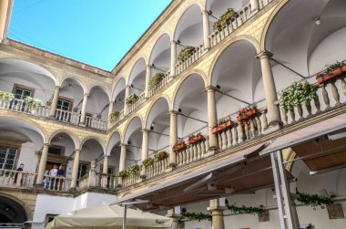 Lviv 'deki güneşli İtalyan Avlusu. Kornyakt Sarayı' nın bir parçası olan sütunları ve kemerleri var. Çiçek kutularıyla balkonlar üst katlarda.
