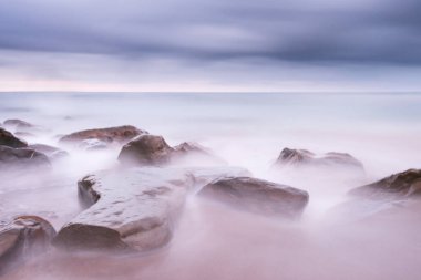 Yumuşak dalgalar yumuşak bir atmosferde taşlara çarpıyor.