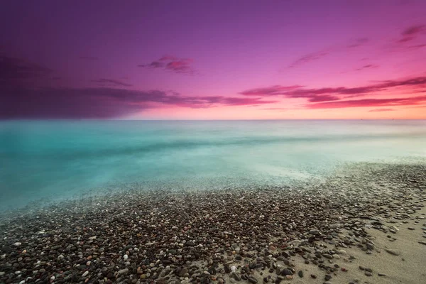 Plajın kumundaki kayaların dokusu pürüzsüz bir deniz ve mor bir gökyüzü.