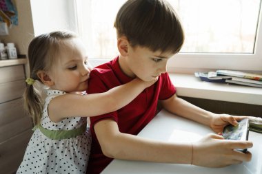 Kardeş ve kardeş mutfakta oturuyor ve telefonda oynuyor