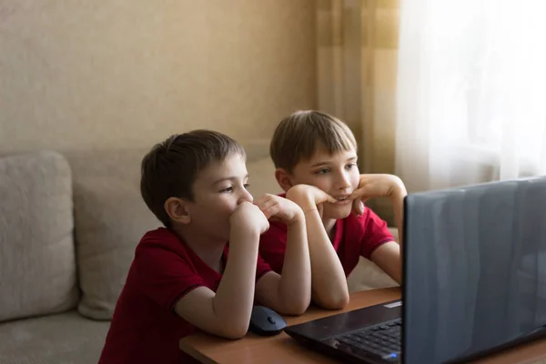 Dos hermanos con camisetas rojas idénticas viendo dibujos animados en la computadora en casa —  Fotos de Stock