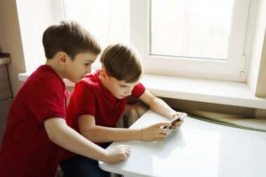 İki kardeş mutfakta oturmuş telefonla oynuyorlar.