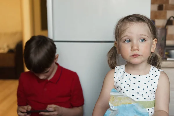 Hermano y hermana en la cocina comiendo y jugando por teléfono . — Foto de Stock