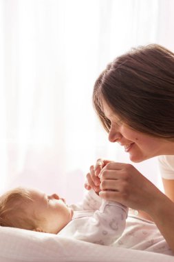 Yeni doğmuş bir bebek yatakta yatıyor ve anne ellerini tutuyor.