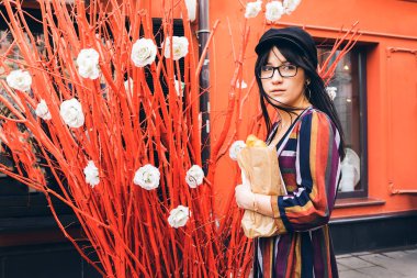 Kızıl duvara karşı parlak elbiseli, uzun saçlı esmer kadın.