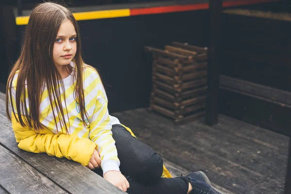 Adolescente en suéter amarillo y jeans negros se sienta en una estructura de madera —  Fotos de Stock