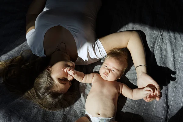 Madre con su hijo recién nacido yacía en la cama bajo los rayos del sol —  Fotos de Stock